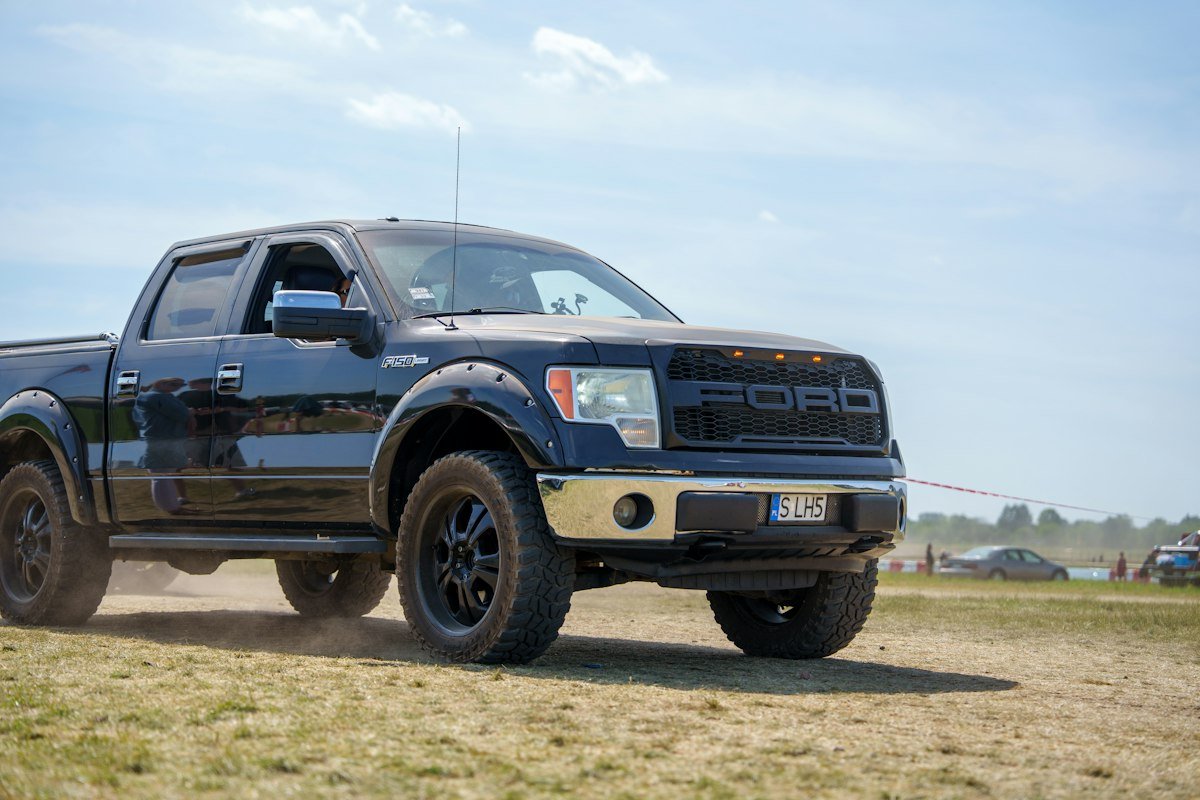 A dark Ford F-150 pickup truck kicking up dust as it drives across an unpaved field